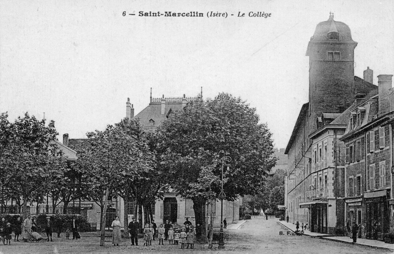 Carte postale ancienne en noir et blanc : la place bordée d'arbres devant le collège de Saint-Marcellin, avec une haute tour à toit en dôme sur la droite, des façades à commerces et un groupe d'enfants et d'adultes posant au premier plan.